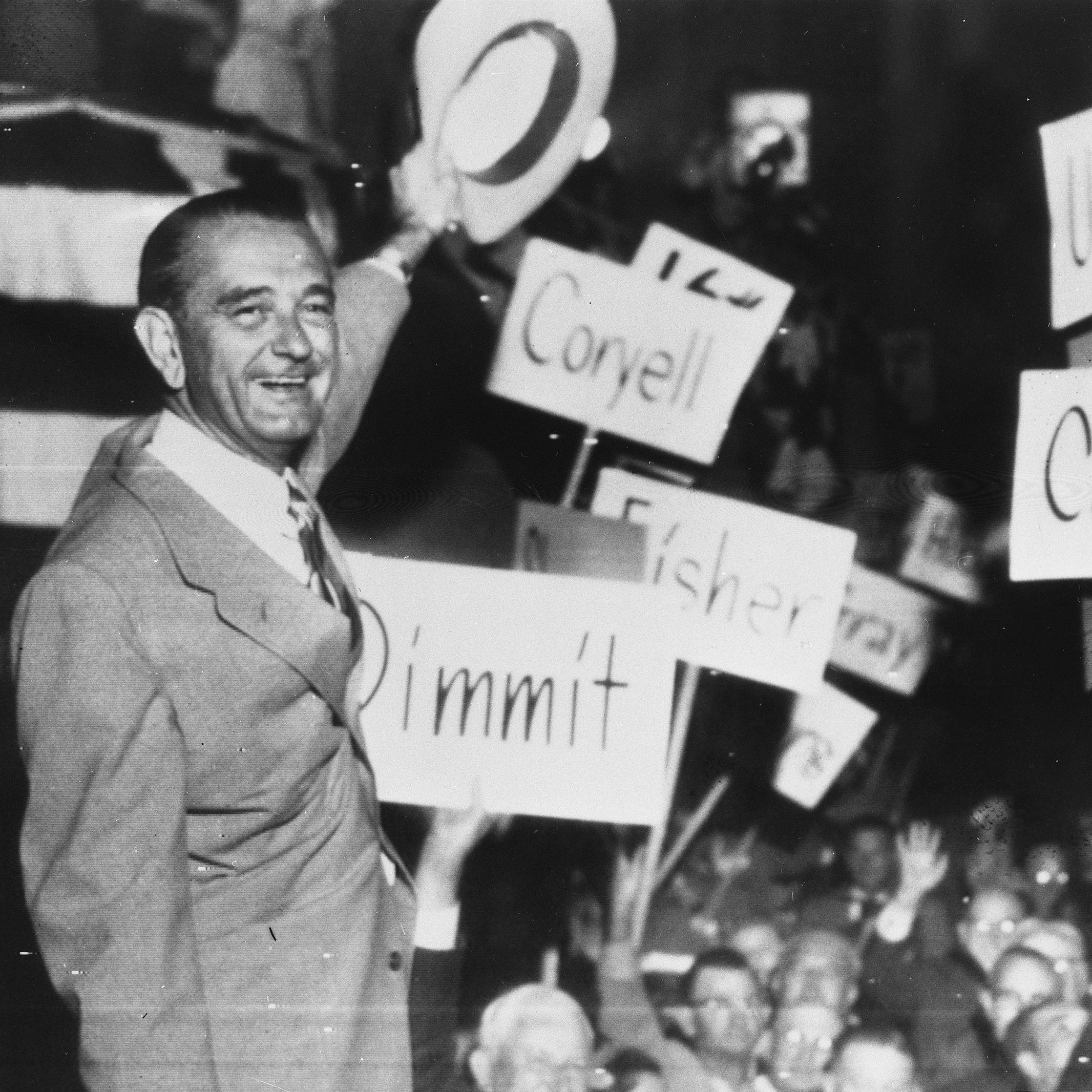 LBJ waves his hat to conventioneers holding signs with names of Texas counties.